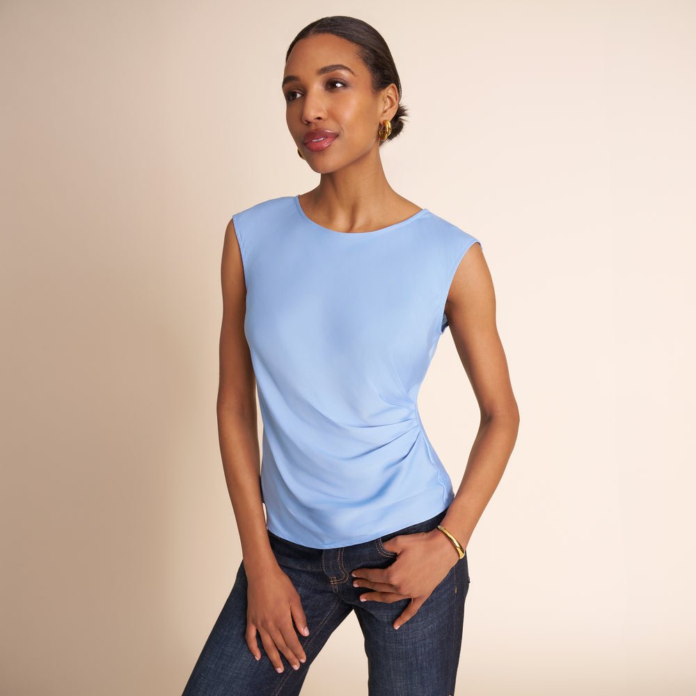 Woman wearing a light blue sleeveless top and jeans on a beige background