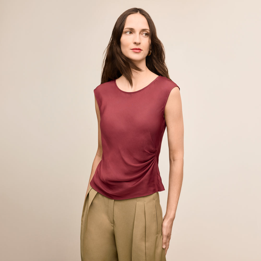 Woman wearing a maroon sleeveless top and beige pants against a beige background