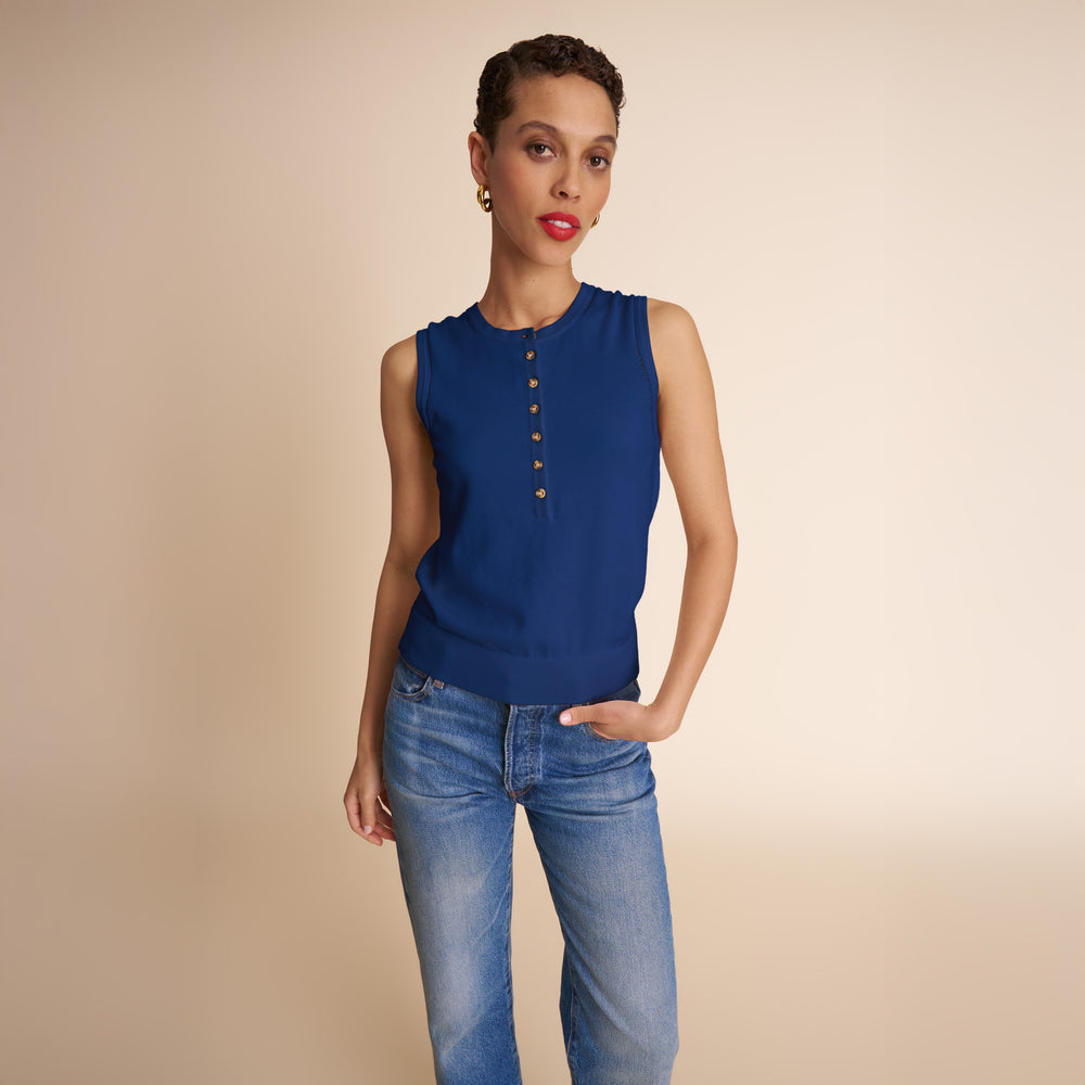 Woman wearing a blue sleeveless top with buttons and jeans on a beige background