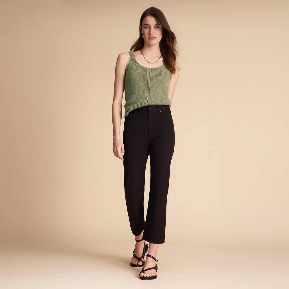 Woman wearing a green tank top and black pants on a beige background