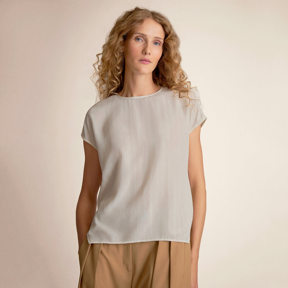 Woman wearing a light-colored top and beige pants against a plain background
