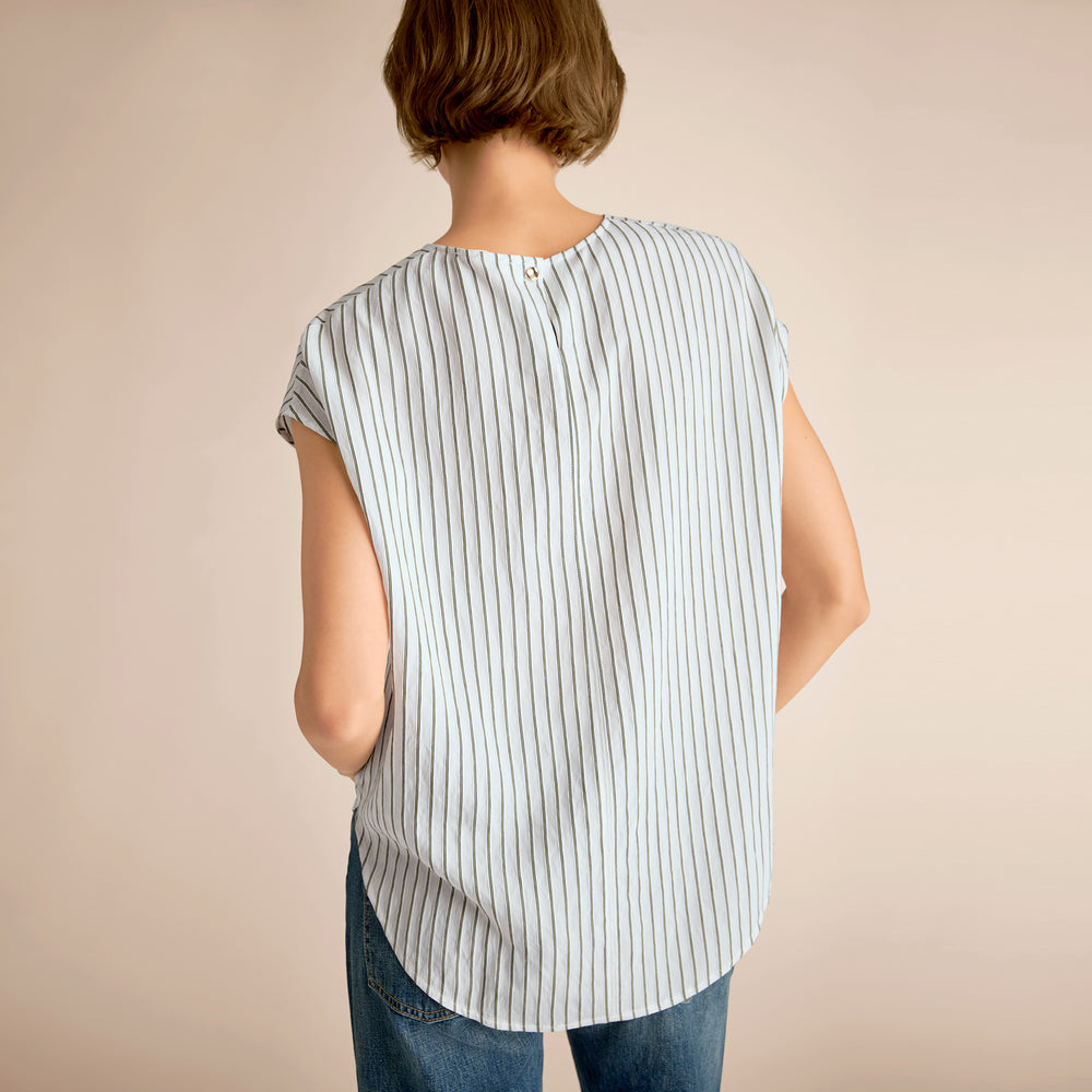 Person wearing a sleeveless striped shirt and jeans on a beige background