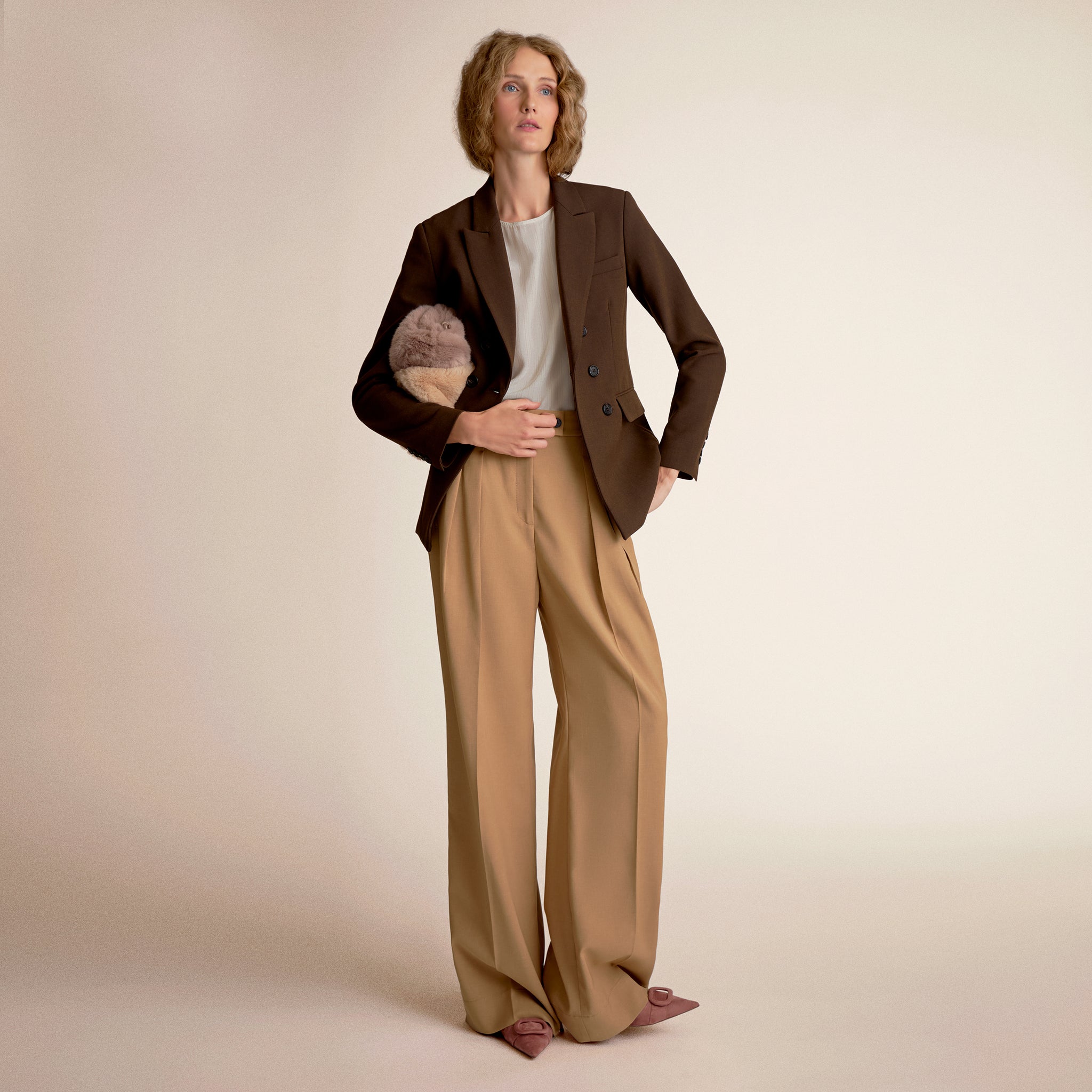 Woman wearing a brown blazer and beige pants on a beige background 