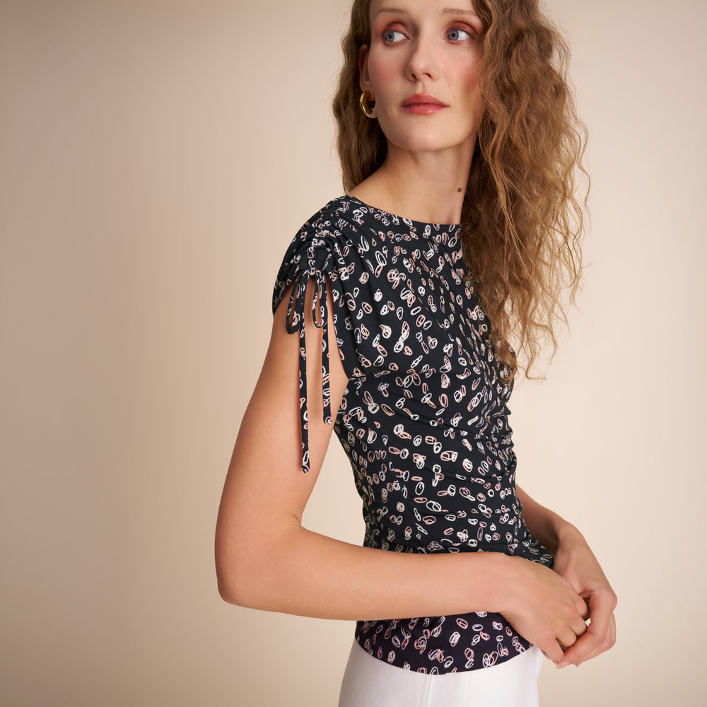 Woman wearing a black floral top with tied sleeves against a beige background