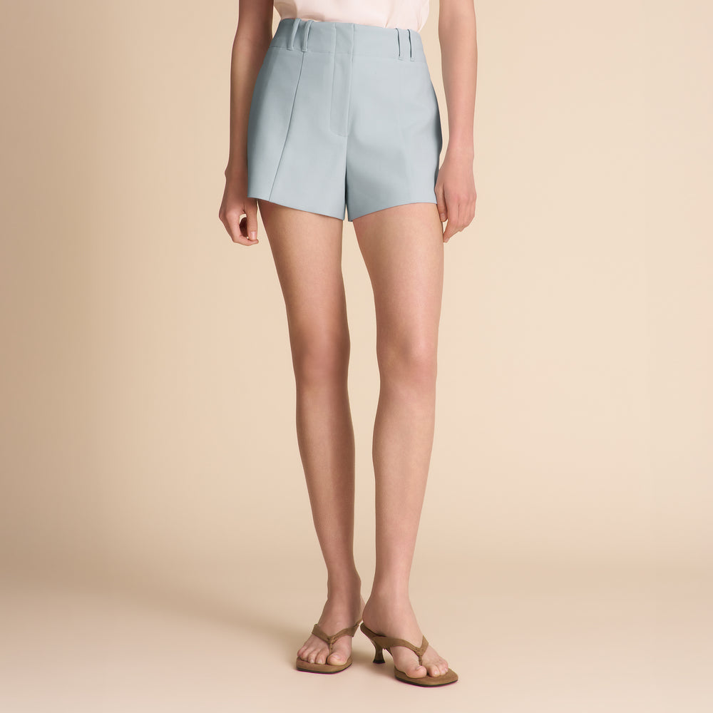 Woman wearing a white tank top and light blue shorts on a beige background