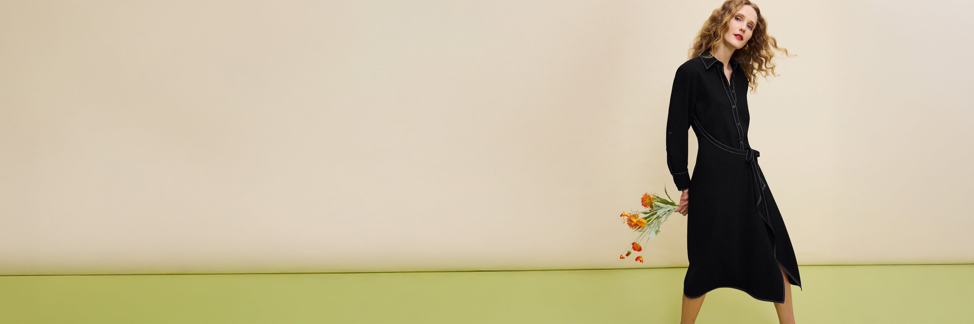 Woman in a black dress holding flowers against a plain background