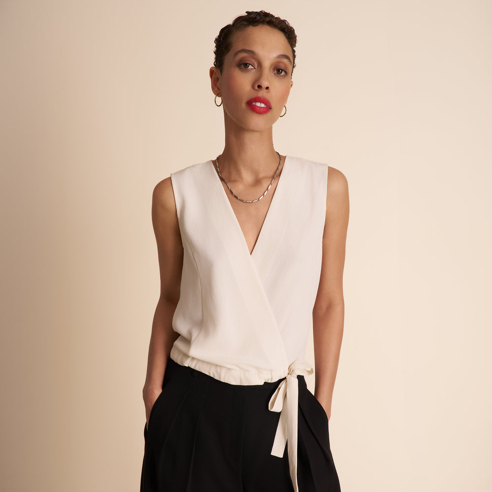 Woman wearing a white sleeveless top with a V-neck and black pants on a beige background