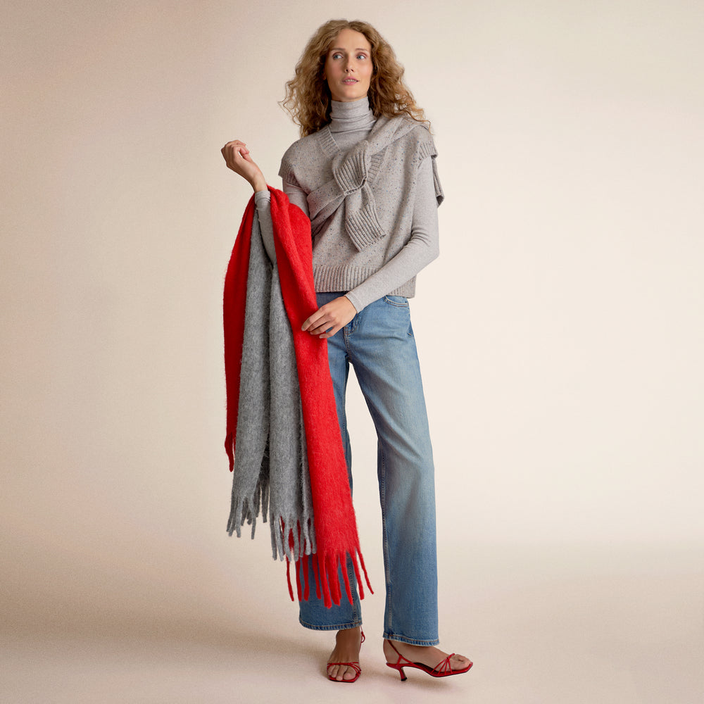 Woman wearing a gray sweater vest holding two scarves