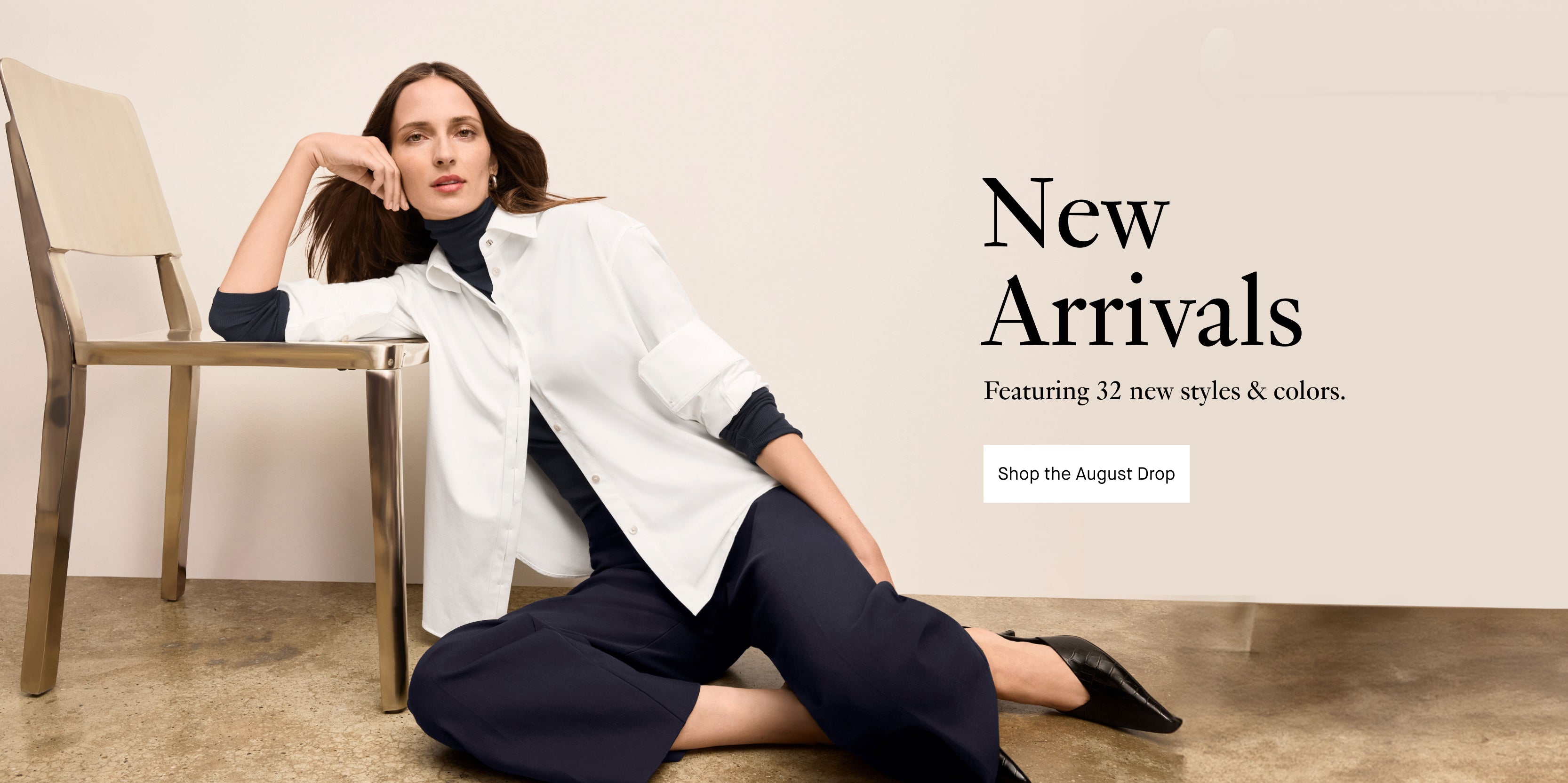 Woman sitting on the floor wearing a white shirt and dark pants with text about new arrivals. "NEW ARRIVALS - FEATURING 32 NEW STYLES & COLORS - SHOP THE AUGUST DROP"