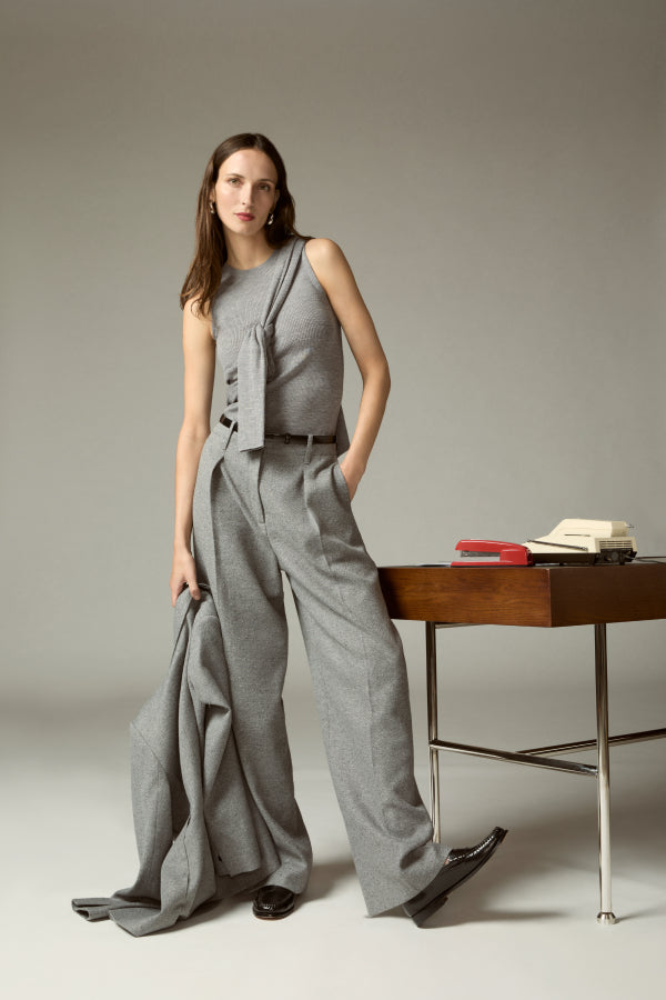 Woman in a gray outfit standing next to a wooden desk with books on it.