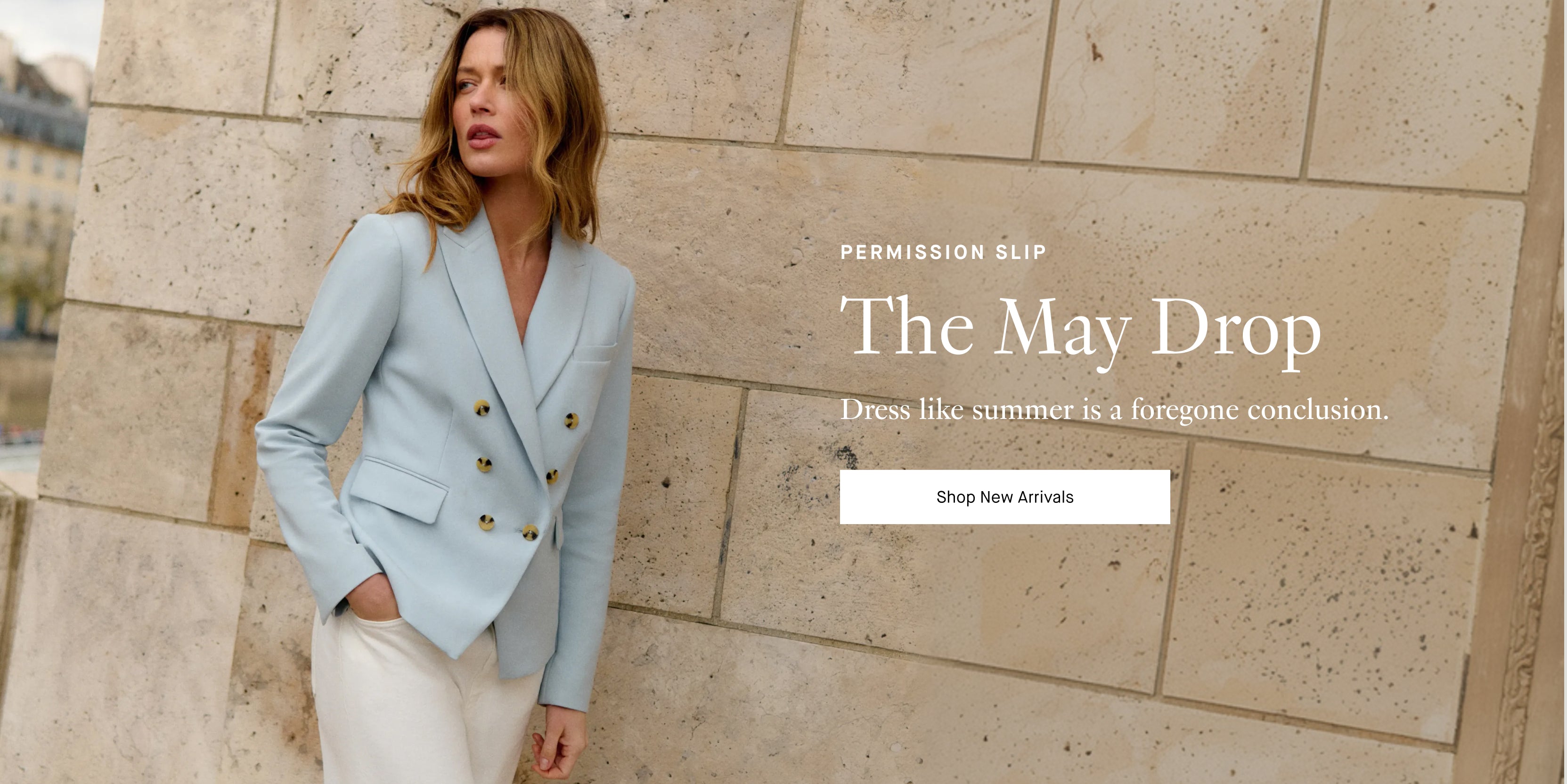 Model wearing a light blue double-breasted blazer and cream pants stands against a stone wall; overlay text reads “PERMISSION SLIP,” “The May Drop,” “Dress like summer is a foregone conclusion.” and a button labeled “Shop New Arrivals.”
