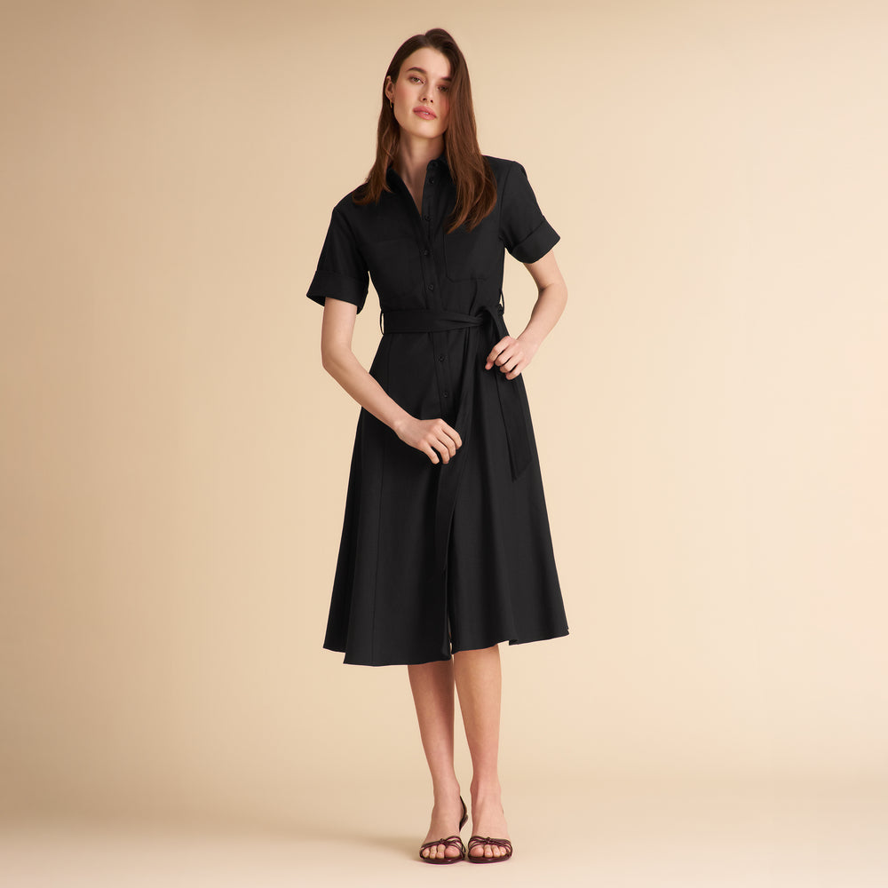 Woman wearing a black dress with a belt against a beige background