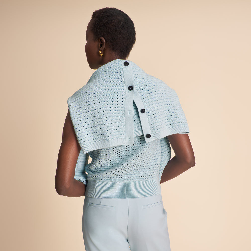 Woman wearing a light blue knitted top with black buttons on a beige background