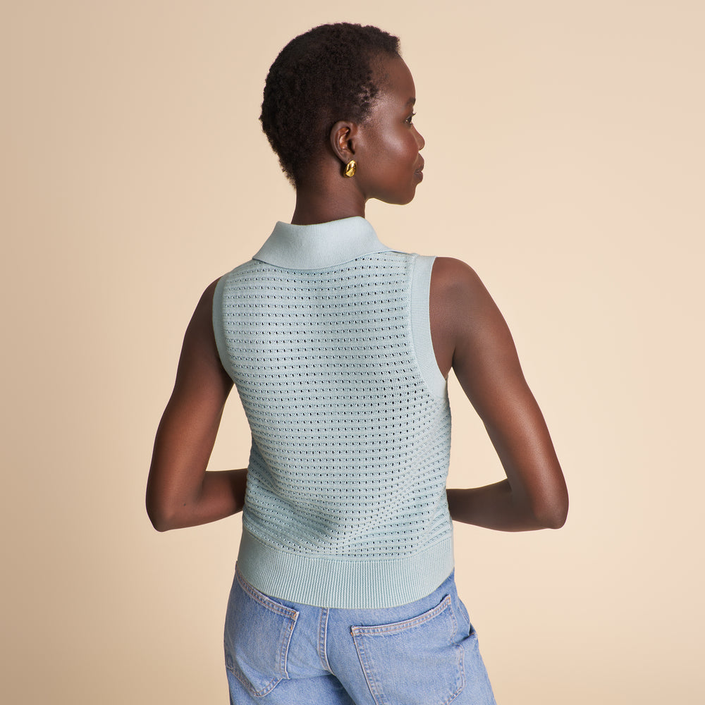 Woman wearing a light blue knitted top with black buttons on a beige background