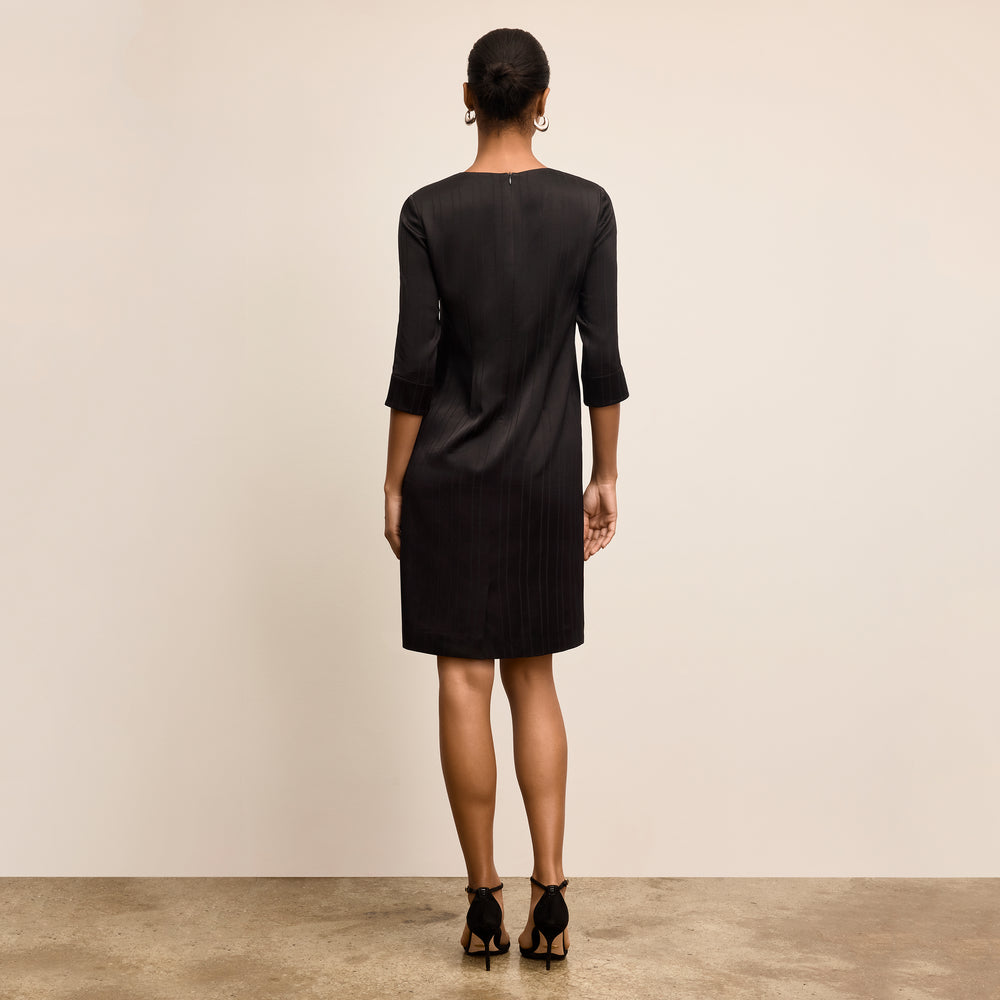 Woman wearing a black dress standing against a plain background