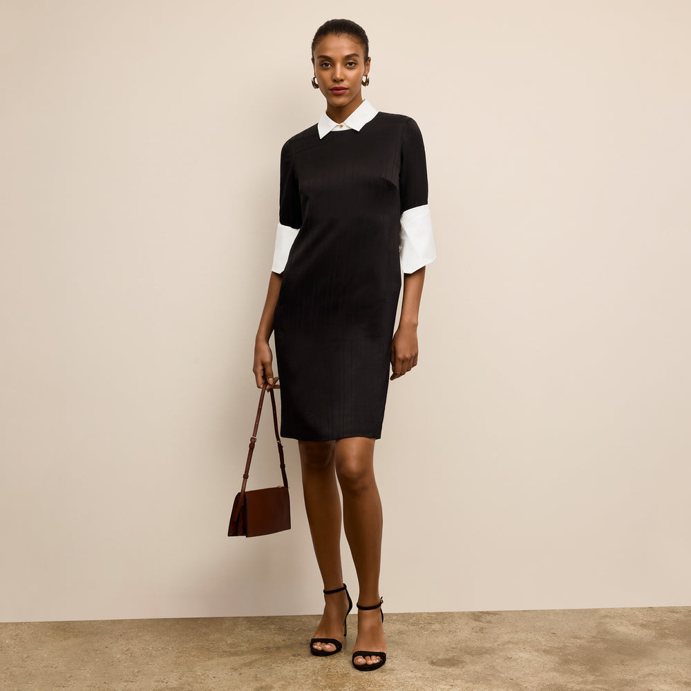 Woman wearing a black and white dress holding a brown handbag against a beige background