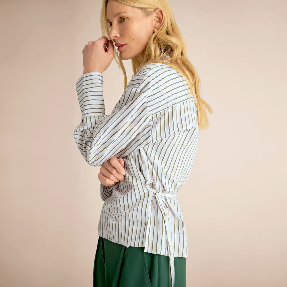 Woman wearing a striped shirt with a tie waist against a beige background