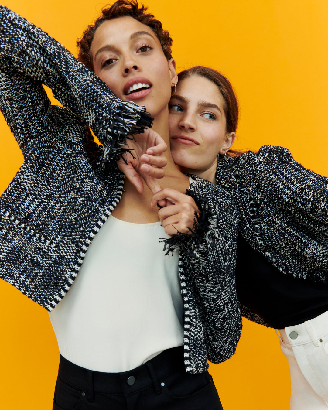 Image of 2 women wearing black and white jackets in front of a bright yellow background
