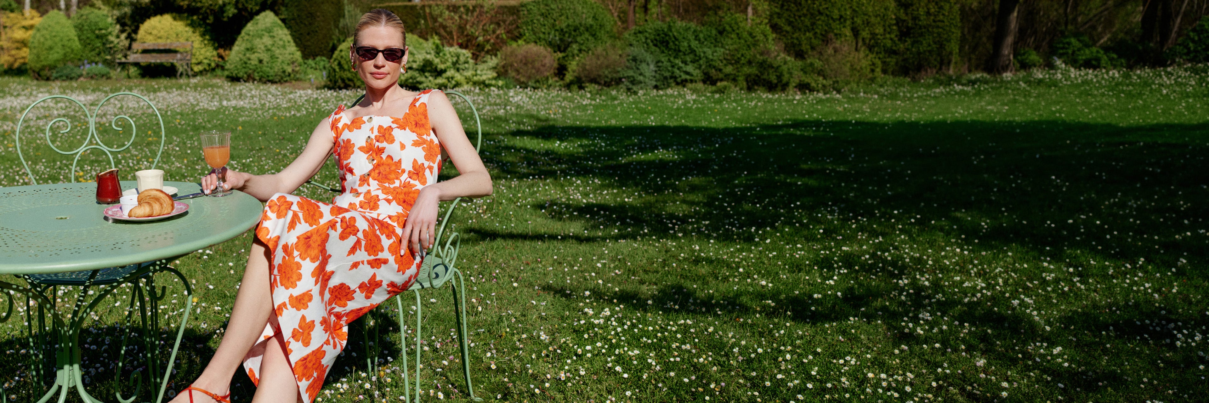 Woman in an orange floral dress sitting at a table in a garden