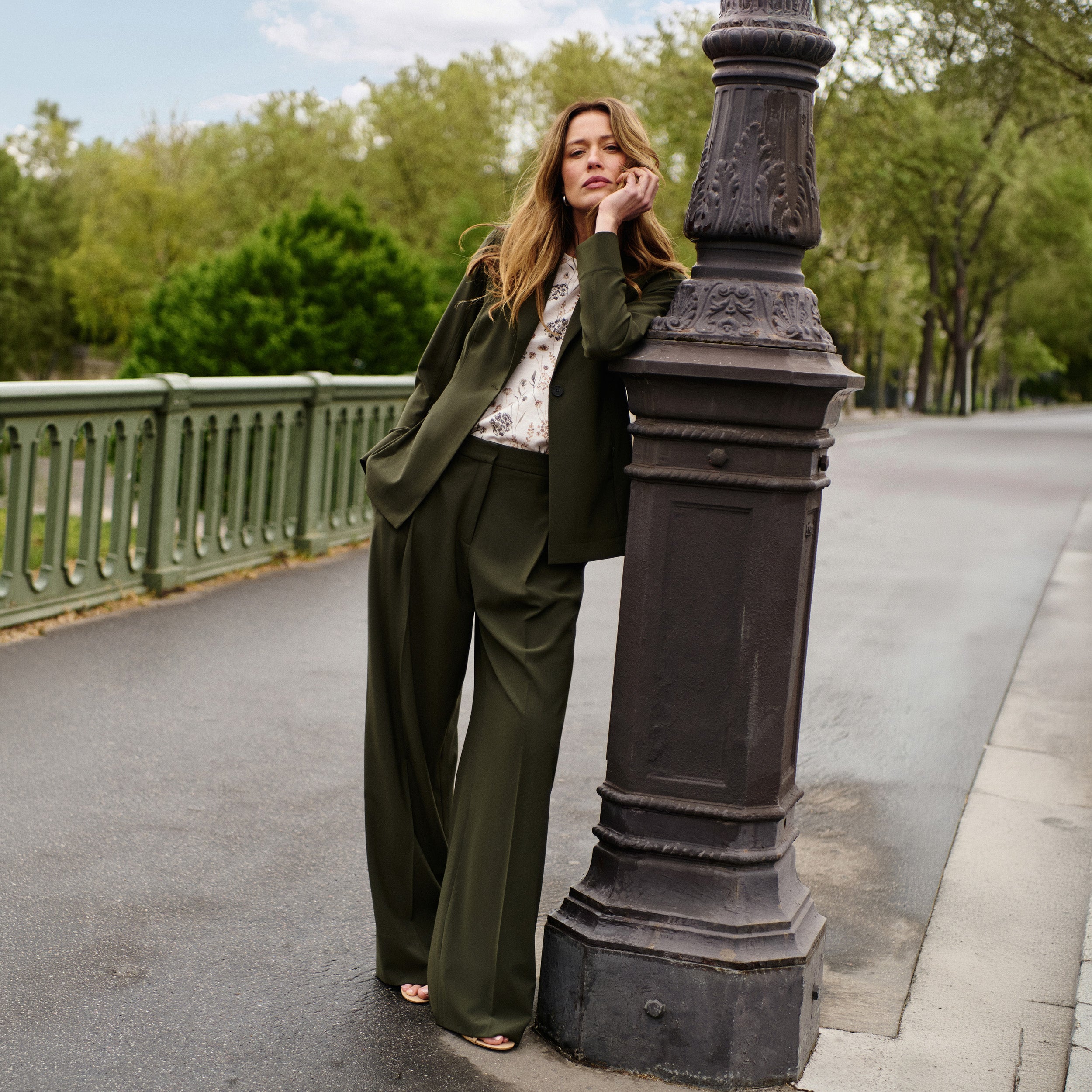 Woman in a green suit standing next to a lamp post on a bridge