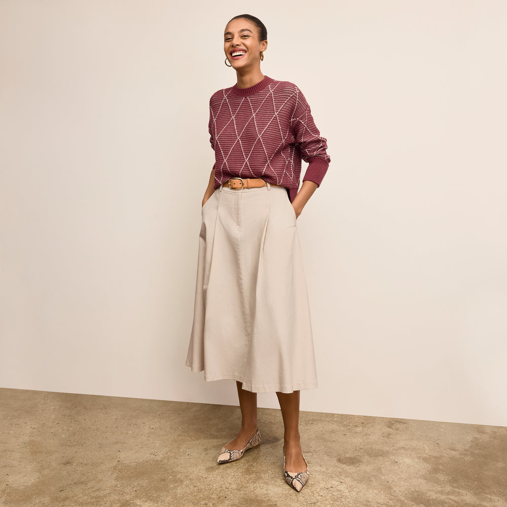 Woman wearing a maroon sweater and beige skirt against a plain background