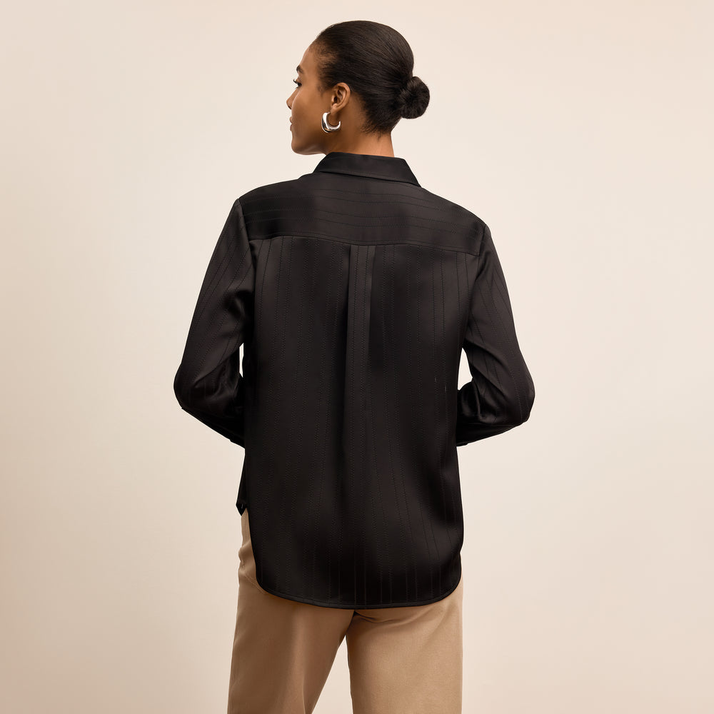Person wearing a black satin shirt with a beige background