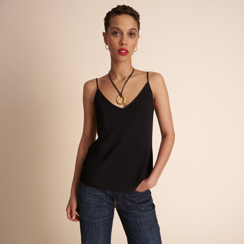 Woman wearing a black tank top and blue jeans against a beige background