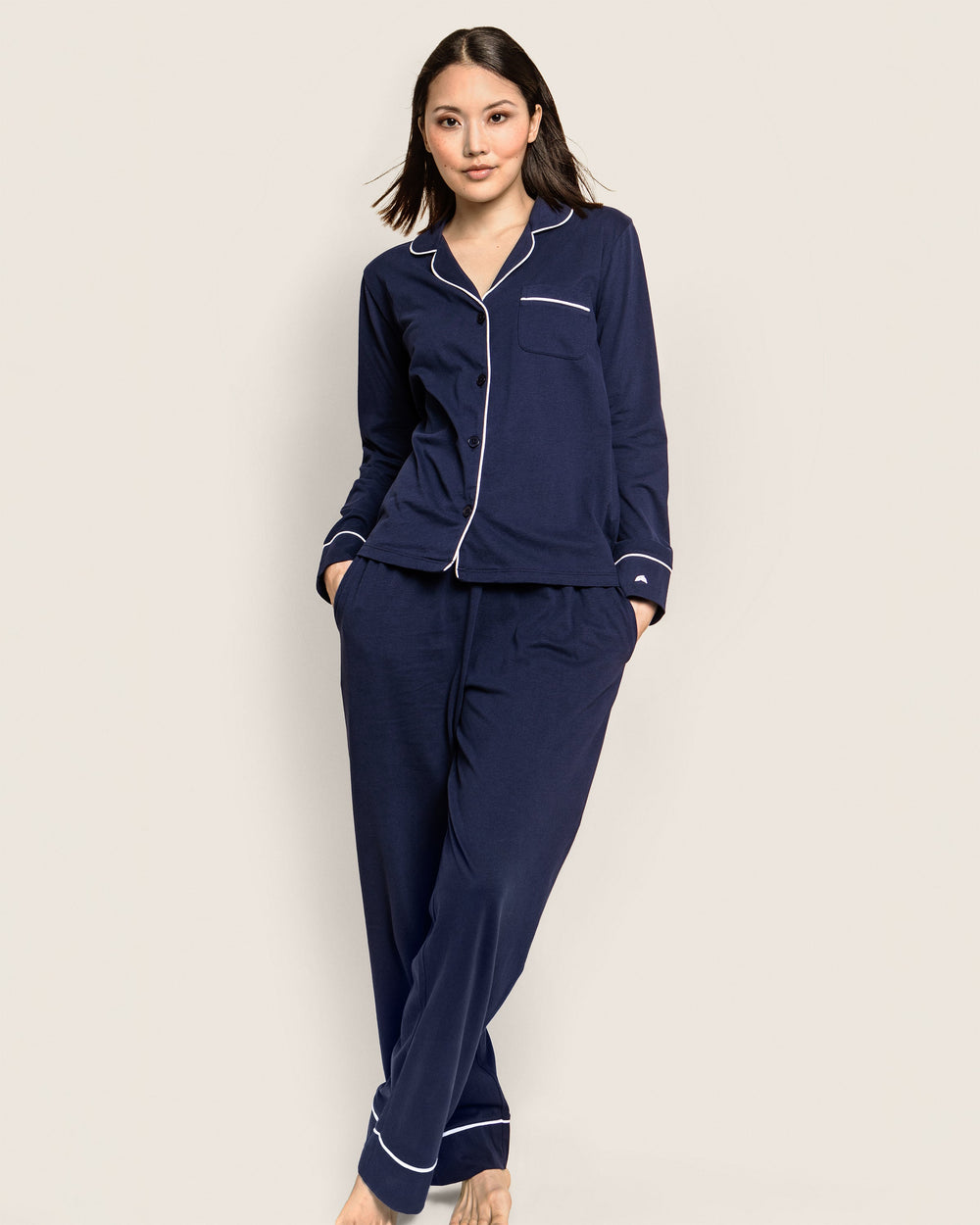 Woman wearing navy pajamas with white piping on a beige background