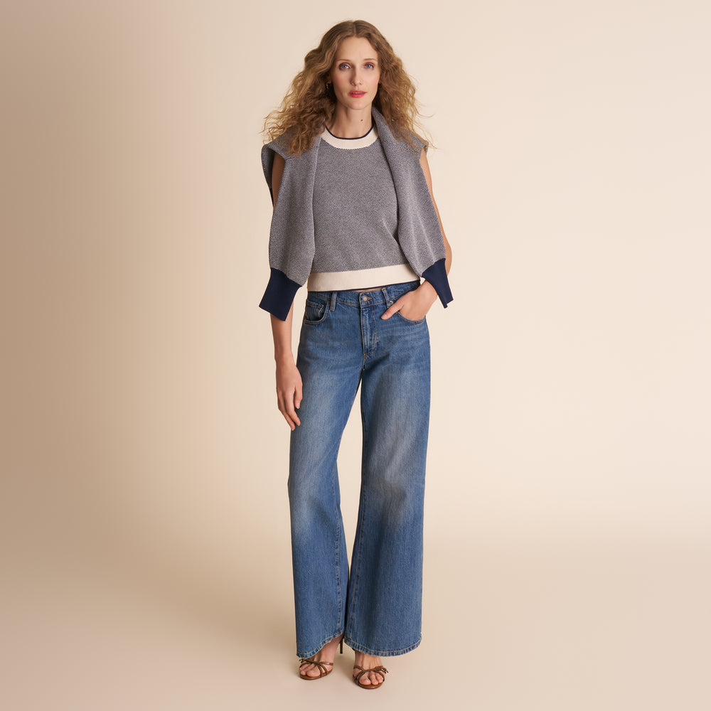 Woman wearing a gray sweater and blue jeans on a beige background
