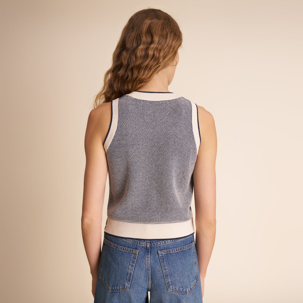 Person wearing a sleeveless patterned top and blue jeans on a beige background