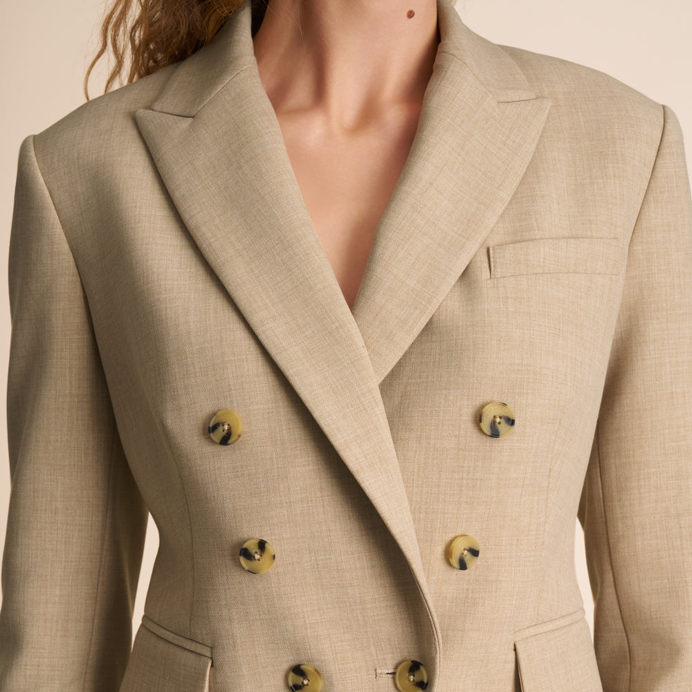 Close-up of a beige double-breasted suit jacket with gold buttons on a neutral background