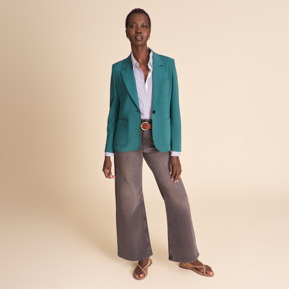 Woman wearing a teal blazer and gray pants on a beige background