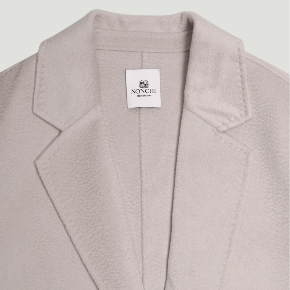 Close-up of a light gray coat with a Nonchi label on a light gray background