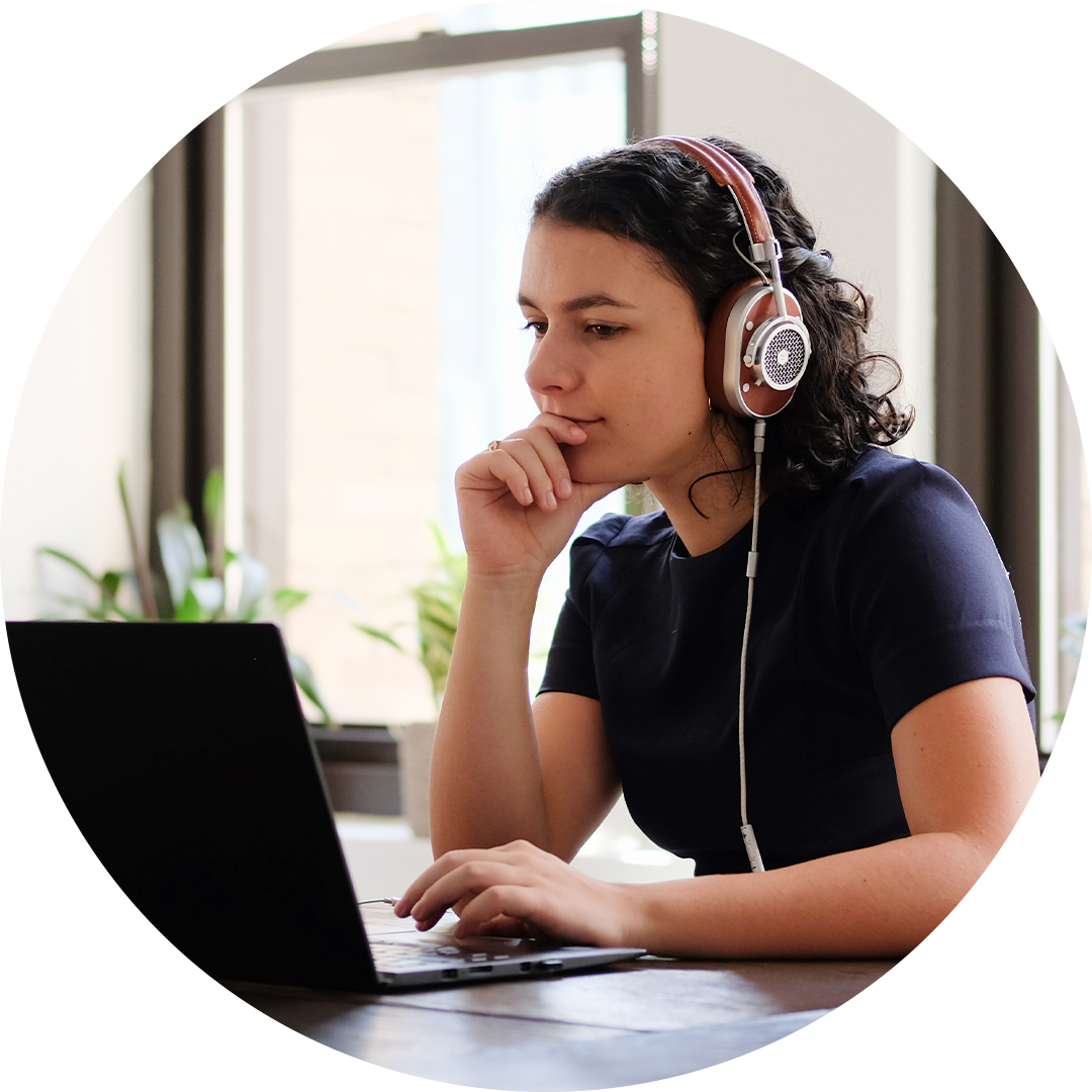 Person wearing headphones and using a laptop at a desk with a window in the background