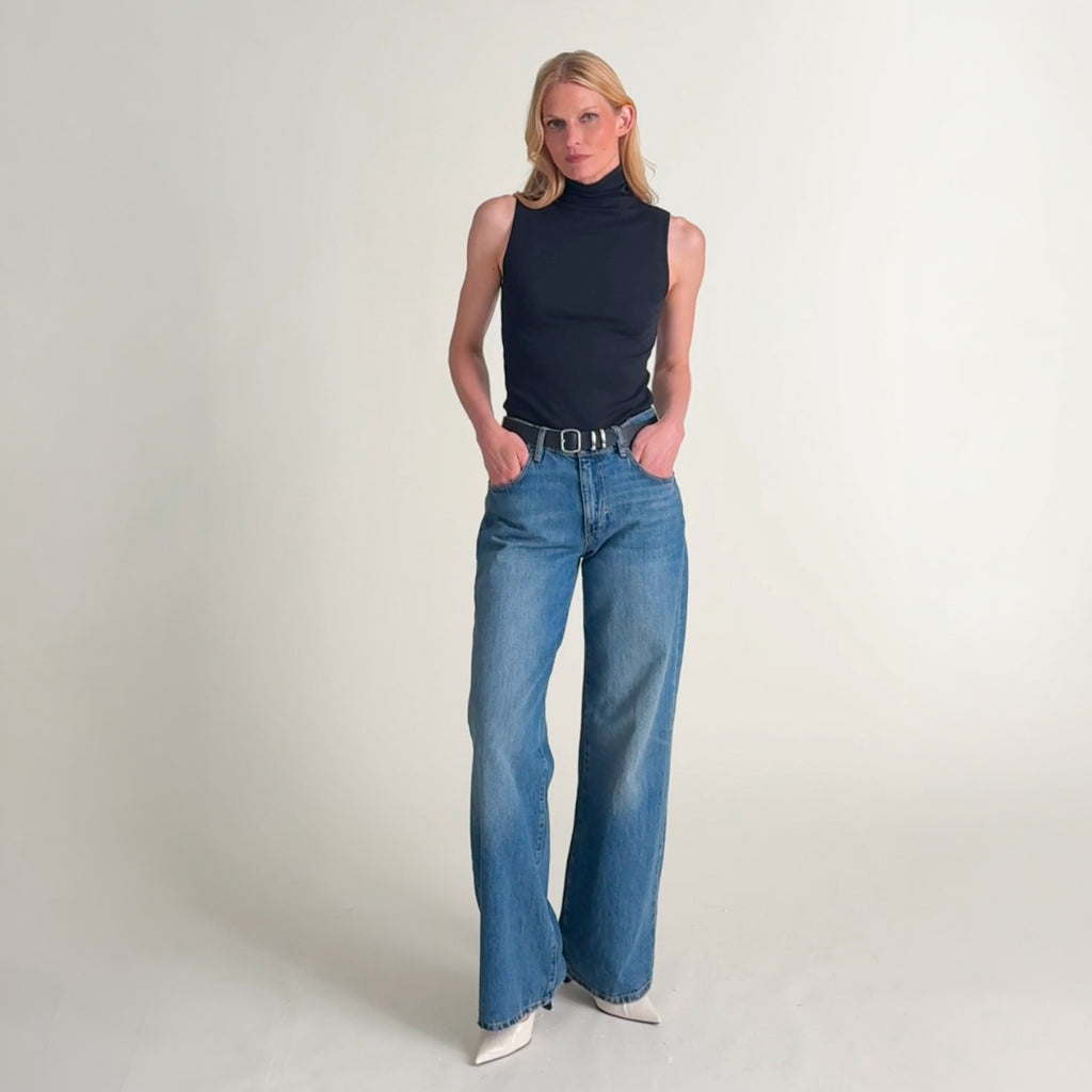 Video of a blonde model wearing a black sleeveless mock-neck top and matching black wide-leg trousers.